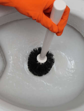 Female hand in orange rubber glove cleaning toilet bowl using brush. Clean up your house.の写真素材