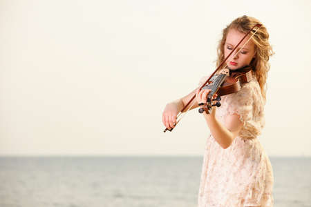 The blonde girl music lover on beach playing the violin. Love of music concept.