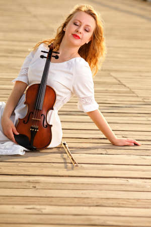 The blonde girl music lover on pier with a violin. Love of music concept.の写真素材