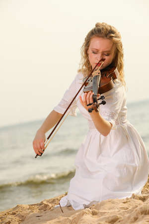 The blonde girl music lover on beach playing the violin. Love of music concept.の写真素材