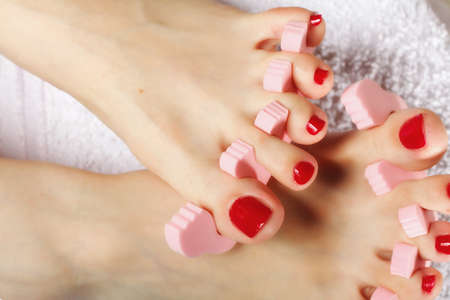 foot pedicure applying woman's feet with red toenails in toe separators
