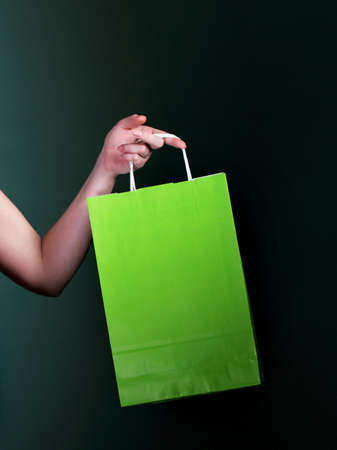 Female hand holding green paper shopping bag on dark backgroundの写真素材