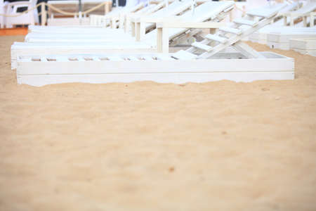 Row of empty white pool plastic chairs deckchairs on sand beach. Vacation conceptの写真素材