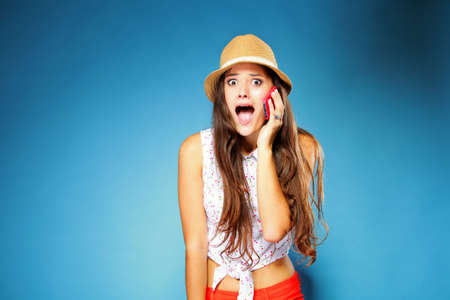 Surprised shocked summer girl talking on mobile phone, blue background