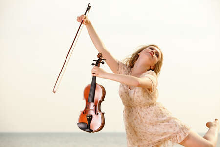 Happy crazy blonde girl music lover on beach with a violin. Love of music concept.の写真素材