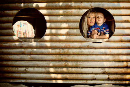 young boy kid or child with mother peeks through hole at playground outdoors at park.の写真素材