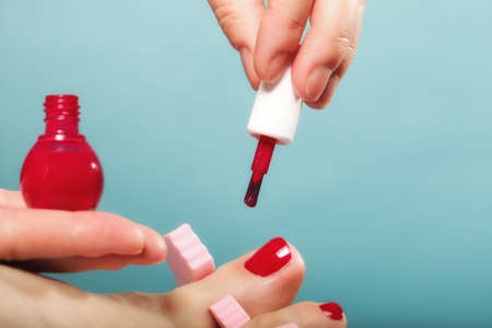 foot pedicure applying woman's feet with red toenails in pink toe separators blue backgroundの写真素材