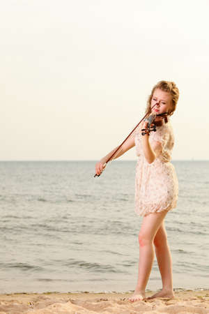 The blonde girl music lover on beach playing the violin. Love of music concept.の写真素材