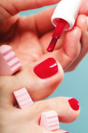 foot pedicure applying woman's feet with red toenails in pink toe separators blue backgroundの写真素材