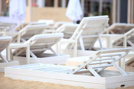 Row of empty white pool plastic chairs deckchairs on sand beach. Vacation conceptの写真素材