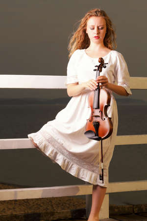 The blonde girl music lover on pier with a violin.  Love of music concept.の写真素材