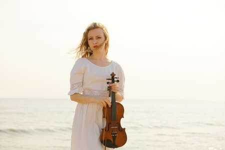 The blonde girl music lover on beach with a violin at sunset or sunrise.  Love of music concept.の写真素材