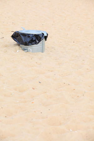 Gray metal garbage bin or trash can with a plastic bag inside beach outdoor