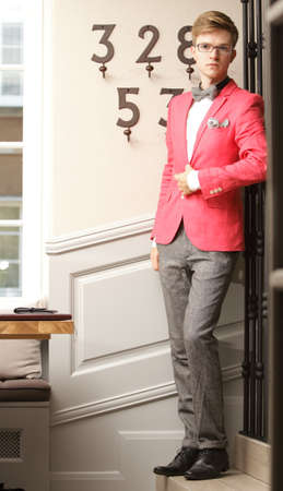 Full length young handsome stylish man fashion model wearning bright red jacket and bow tie posing indoorの写真素材