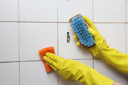 gloved hand cleaning dirty old tiles with brush in a bathroom