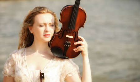 Portrait of blonde girl music lover on beach with a violin. Love of music concept.