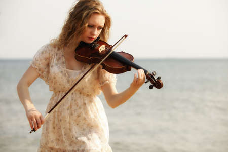 Portrait of blonde girl music lover on beach playing the violin. Love of music concept.の写真素材