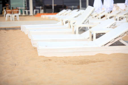 Row of empty white pool plastic chairs deckchairs on sand beach. Vacation conceptの写真素材