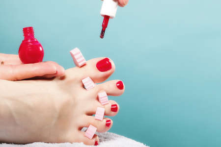 foot pedicure applying woman's feet with red toenails in pink toe separators blue background