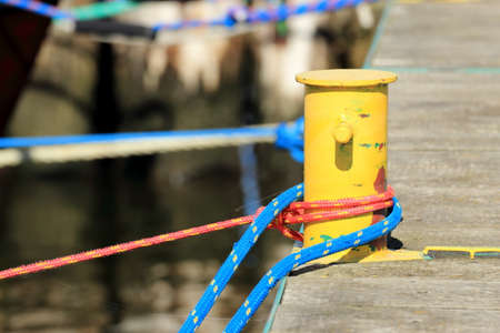 harbor quayside old yellow mooring bollard with blue red rope in marina