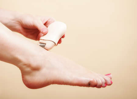 woman shaving her legs with electric shaver depilation on orange. Beauty and skin body care concept.の写真素材