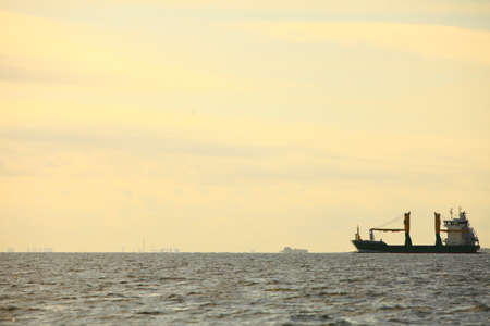 Transportation, cargo conteiner ship sailing in still water heading for the port against sunset sky