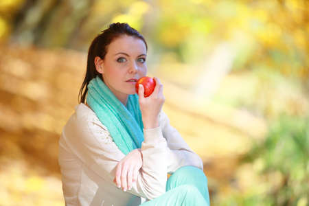 Fall lifestyle concept, harmony freedom. Casual young woman girl relaxing in autumnal park eating red apple. Golden colorful leaves backgroundの写真素材