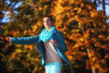 Happiness carefree and autumn. Young woman having fun blowing soap bubbles in park on a bright yellow leaves backgroundの写真素材