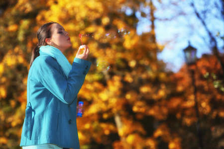 Happiness carefree and autumn. Young woman having fun blowing soap bubbles in park on a bright yellow leaves backgroundの写真素材