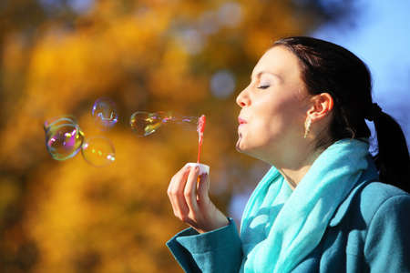 Happiness carefree and autumn. Young woman having fun blowing soap bubbles in park on a bright...