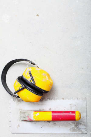 Ear hearing protection. Yellow working protective headphones noise muffs, and notched trowel, toolwork in construction siteの写真素材