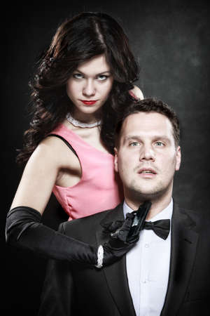 Detective theme. Retro style attractive couple, rich gangster and charming woman sexy detective spy with gun on black backgroundの写真素材