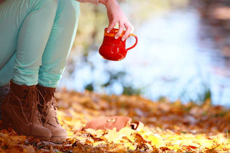Woman relaxing in the autumn park enjoying hot drink coffee or tea, female hand holding red mug with...
