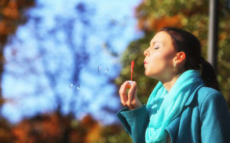 Happiness carefree and autumn. Young woman having fun blowing soap bubbles in park on a bright...
