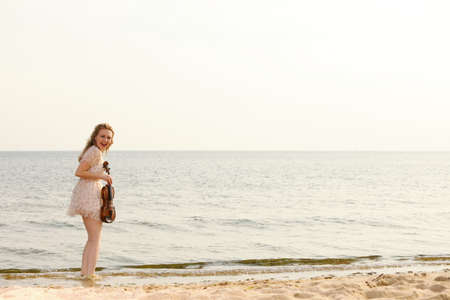 Happy crazy blonde girl music lover on beach with a violin.の写真素材