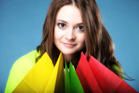 young woman in bright vivid colour sweater with paper multi coloured shopping bags on blue...