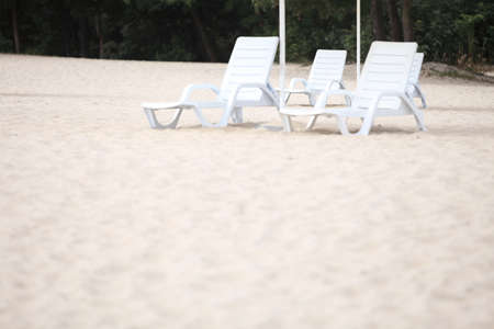 empty white pool plastic chairs deckchairs on sand beach. Vacation concept