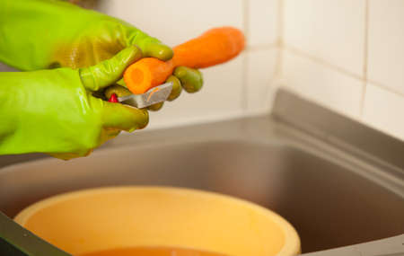 Woman hands in green gloves slicing preparing carrots in kitchen, indoor. Healthy diet, organic nutrition. Realistic, natural image.の写真素材