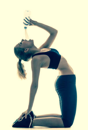 Full length beautiful sporty woman doing stretching exercise drinking water camel pose in silhouette...