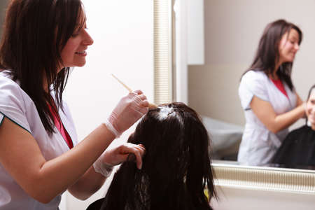 Brunette woman in hairdressing beauty salon. Girl dying hair by hairstylist. hairdresser colouring client hair.の写真素材