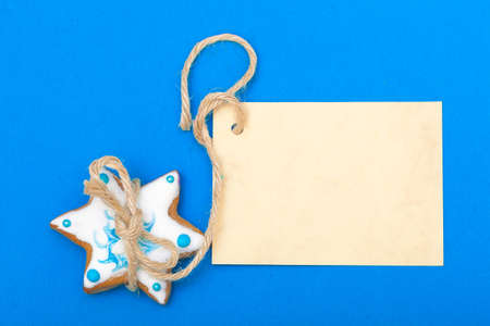 Homemade gingerbread cake star with icing and blue decoration and blank paper card copy-space on blue as christmas background. Holiday handmade concept.の写真素材