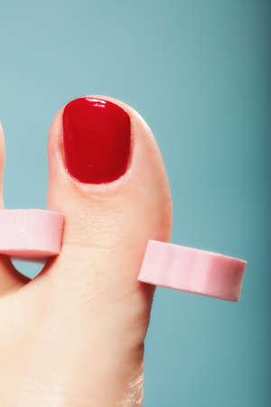 foot pedicure applying woman's feet with red toenails in pink toe separators blue background