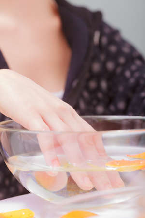 Close up of female hand soaking in glass bowl of water. Manicure and skincare. Woman in spa beauty...
