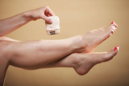 woman shaving her legs with electric shaver depilation body care on orange. Beauty and skin care concept.の写真素材