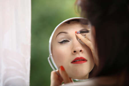 Young woman preparing to party indoor, girl retro style applying make up with brush looking at mirror green blurred backgroundの写真素材