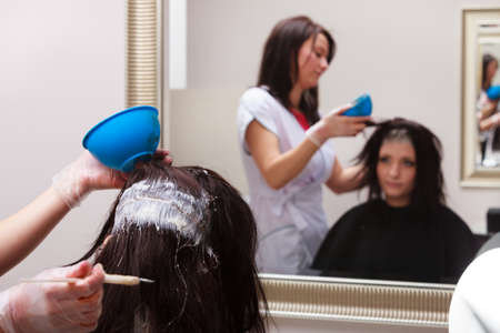 Brunette young woman in hairdressing beauty salon. Girl dying hair by hairstylist. hairdresser colouring client hair.の写真素材