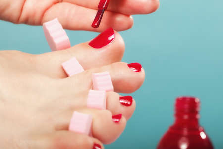 foot pedicure applying woman's feet with red toenails in pink toe separators blue backgroundの写真素材