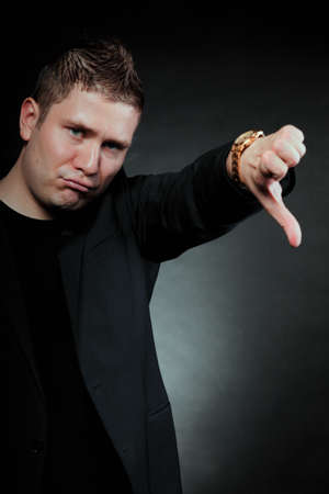 disappointed young man showing thumb down hand sign looking with negative expression disapproval on...