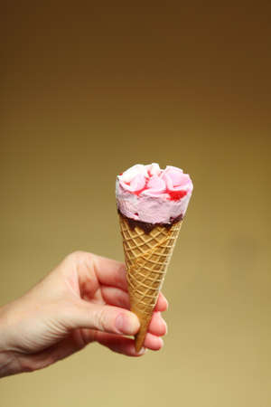 Berry icecream waffle cone in hand on brown. Refreshing dessert for summertime.