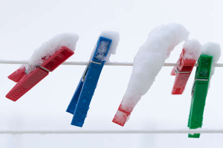 Colorful clips for washing laundry covered with snow on strip rope outdoor. Winter housework concept.の写真素材
